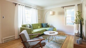 Una sala de estar con un sofá verde, una silla de madera, una mesa de centro redonda y una lámpara de pie.