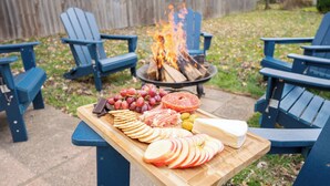 Un montaje para picnic con una mesa de madera, sillas Adirondack azules y un brasero al fondo.