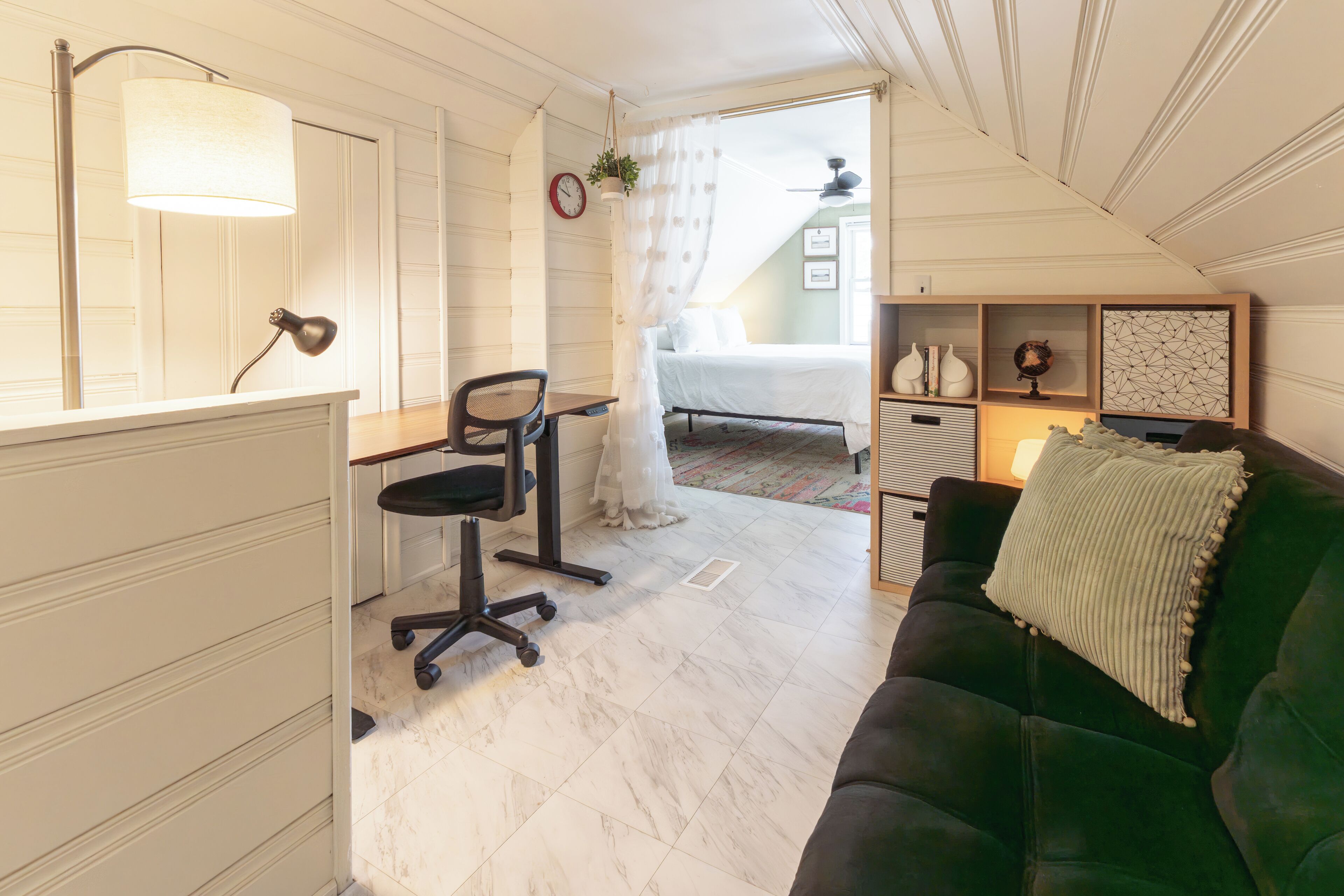 A room with a desk, office chair, green sofa, and a bed with a white canopy.
