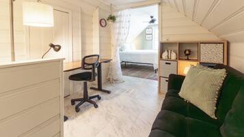 A room with a desk, office chair, green sofa, and a bed with a white canopy.