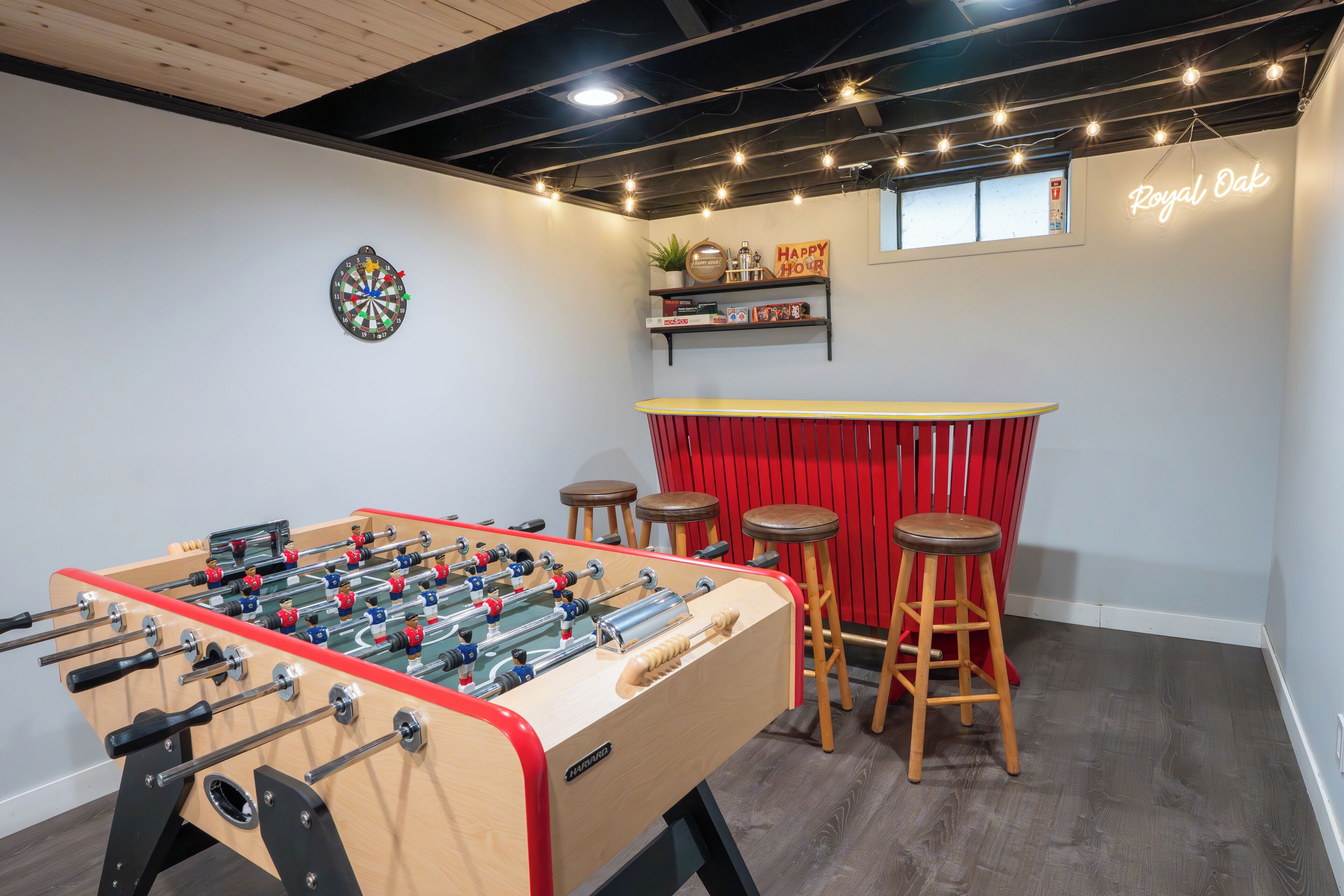 Una habitación con mesa de fútbol de mesa, taburetes, dardo y un letrero de neón que dice 'Royal Oak'.