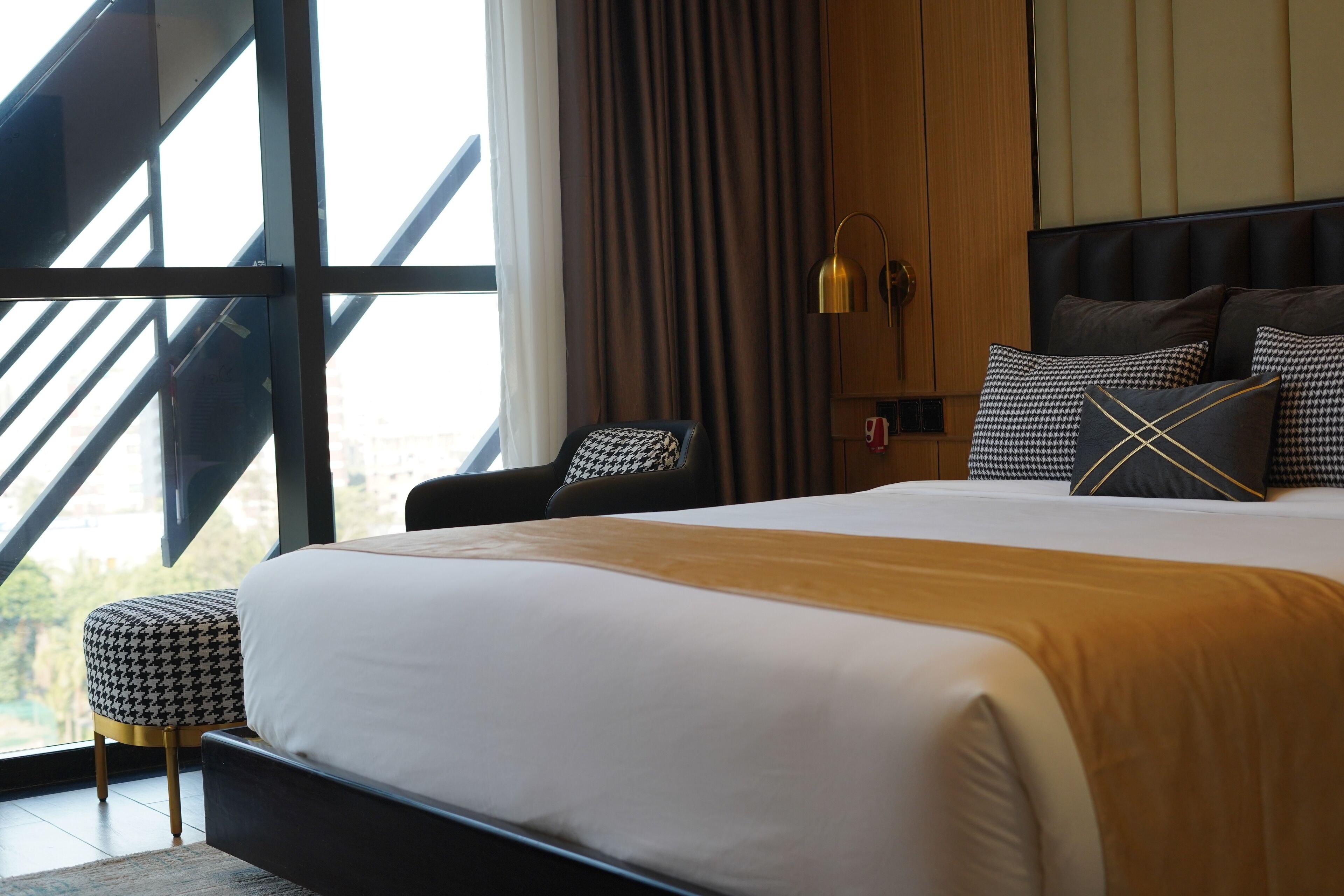 Una camera d'albergo moderna con un letto grande, una zona salotto con una poltrona e poggiapiedi, un comodino e vista attraverso un'ampia finestra.