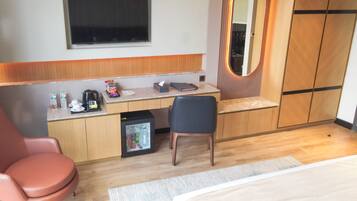 Una habitación de hotel con cama, escritorio con silla, refrigerador pequeño, espejo y ventana.