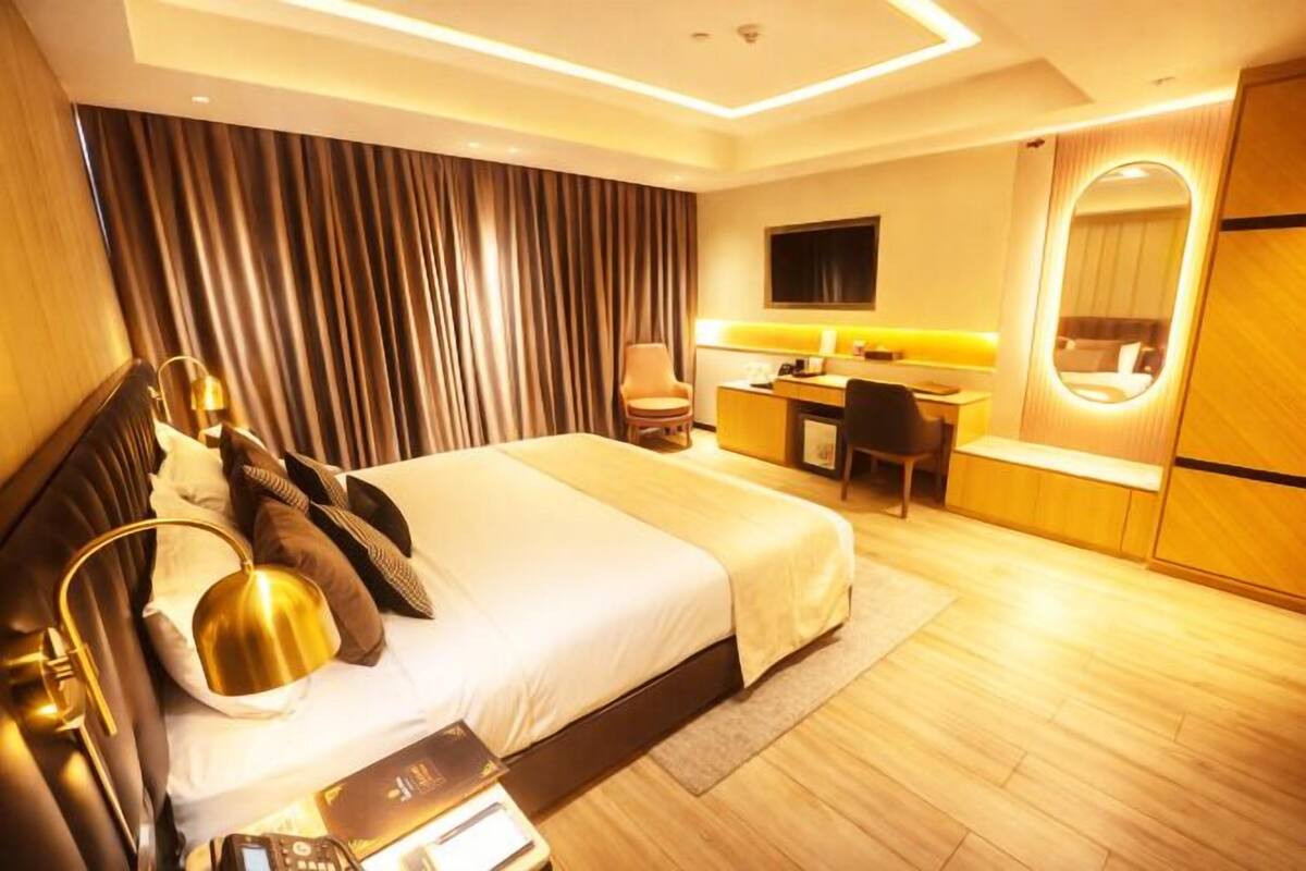 A modern hotel room with a large bed, a desk, and a mirror.