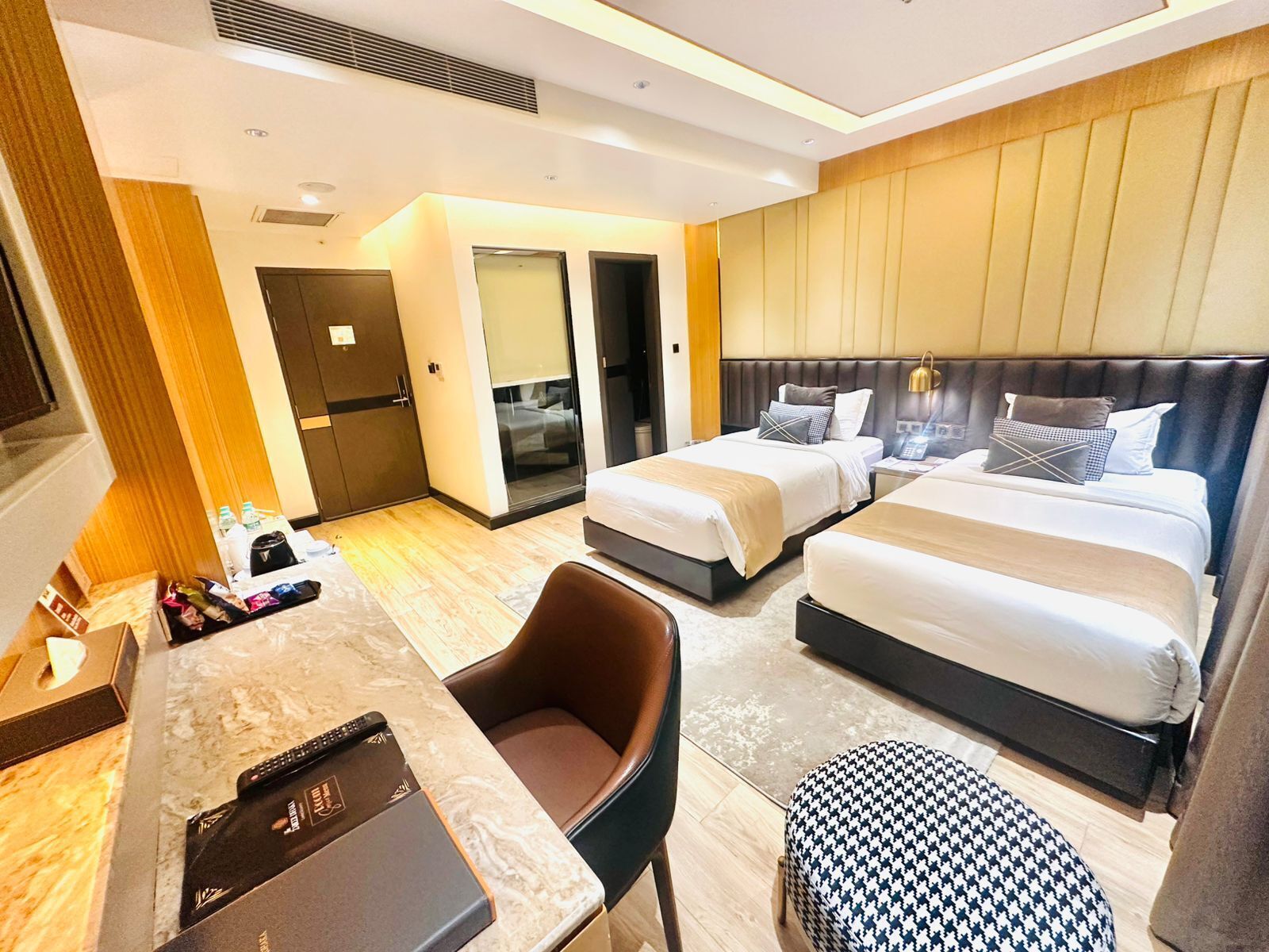 A hotel room with two beds, a desk, a chair, and a small ottoman.