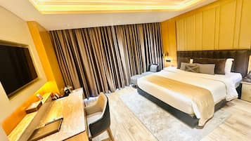 A hotel room with a bed, a desk, a chair, a TV, and a curtain.