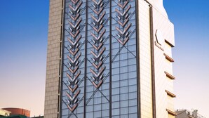 Un edificio alto con un llamativo diseño en zigzag en su fachada, múltiples balcones y un cielo azul despejado al fondo.
