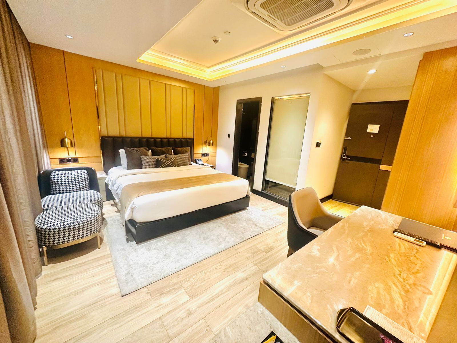 A modern hotel room with a large bed, a desk, a chair, and a wardrobe.