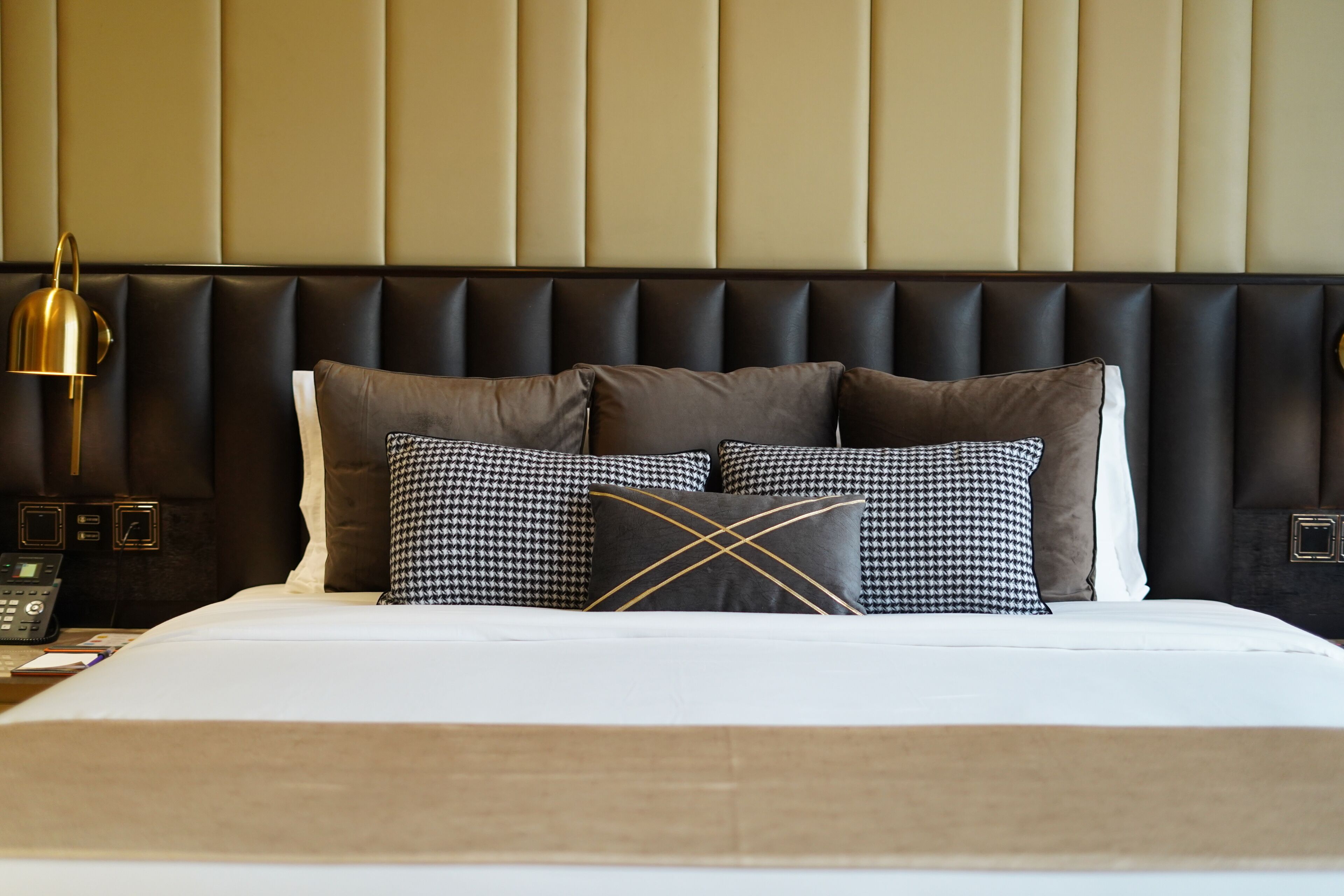 A hotel room with a bed, a headboard, and a bedside table with a lamp and phone.