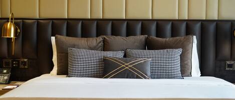 A hotel room with a bed, a headboard, and a bedside table with a lamp and phone.