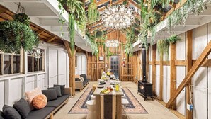 A cozy, rustic room with a wooden ceiling, hanging plants, a central table with a rug, a sofa, and a fireplace. - Multi-Family Haven! 22ppl, Hot Tub, Golf (Pleasant View)