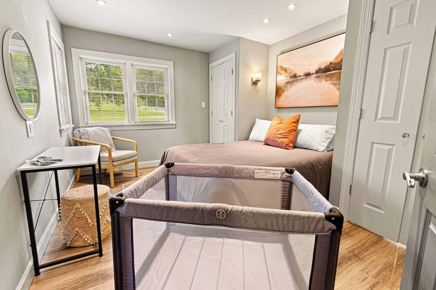 A bedroom with a bed, a chair, a table, a window with blinds, and a door.