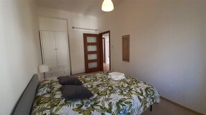 Ein Schlafzimmer mit einem Bett, einem Kleiderschrank, einem Spiegel und einer Tür zu einem anderen Raum.