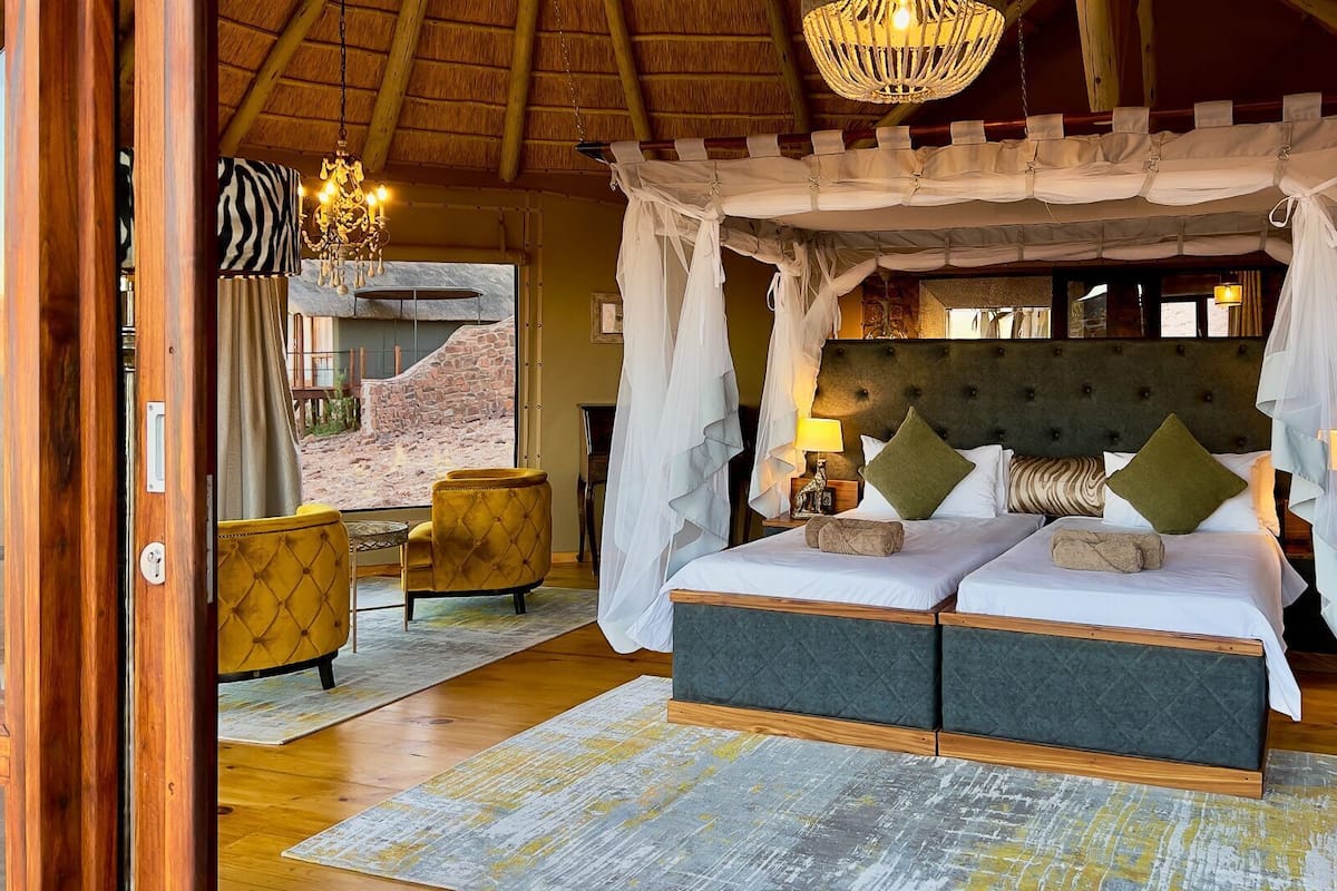 A bedroom with a four-poster canopy bed, a stone wall, and a view of the outdoors.