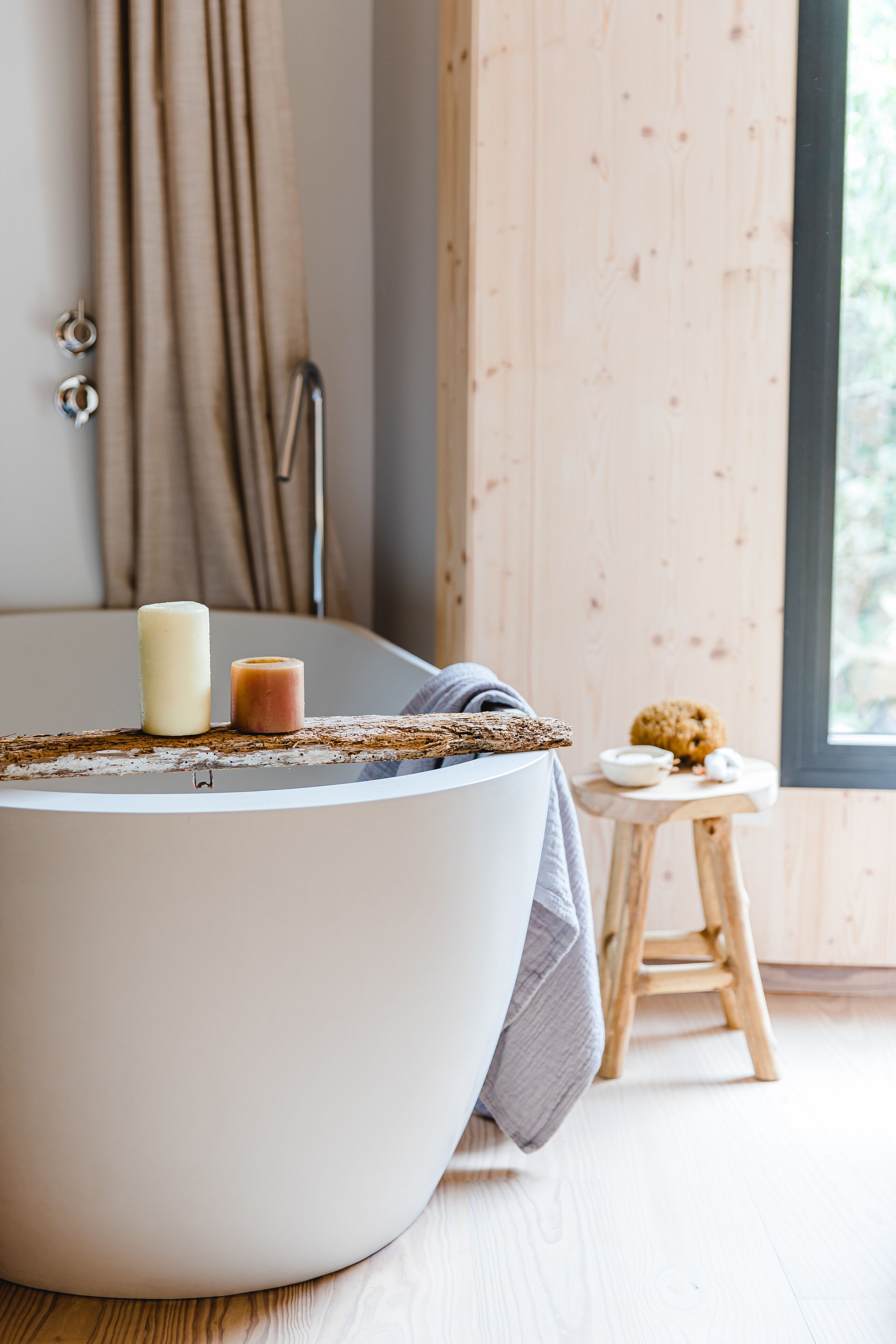 A modern bathroom with a round bathtub, a candle, and a small wooden stool with a bowl and a cookie.