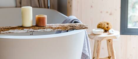 A modern bathroom with a round bathtub, a candle, and a small wooden stool with a bowl and a cookie.