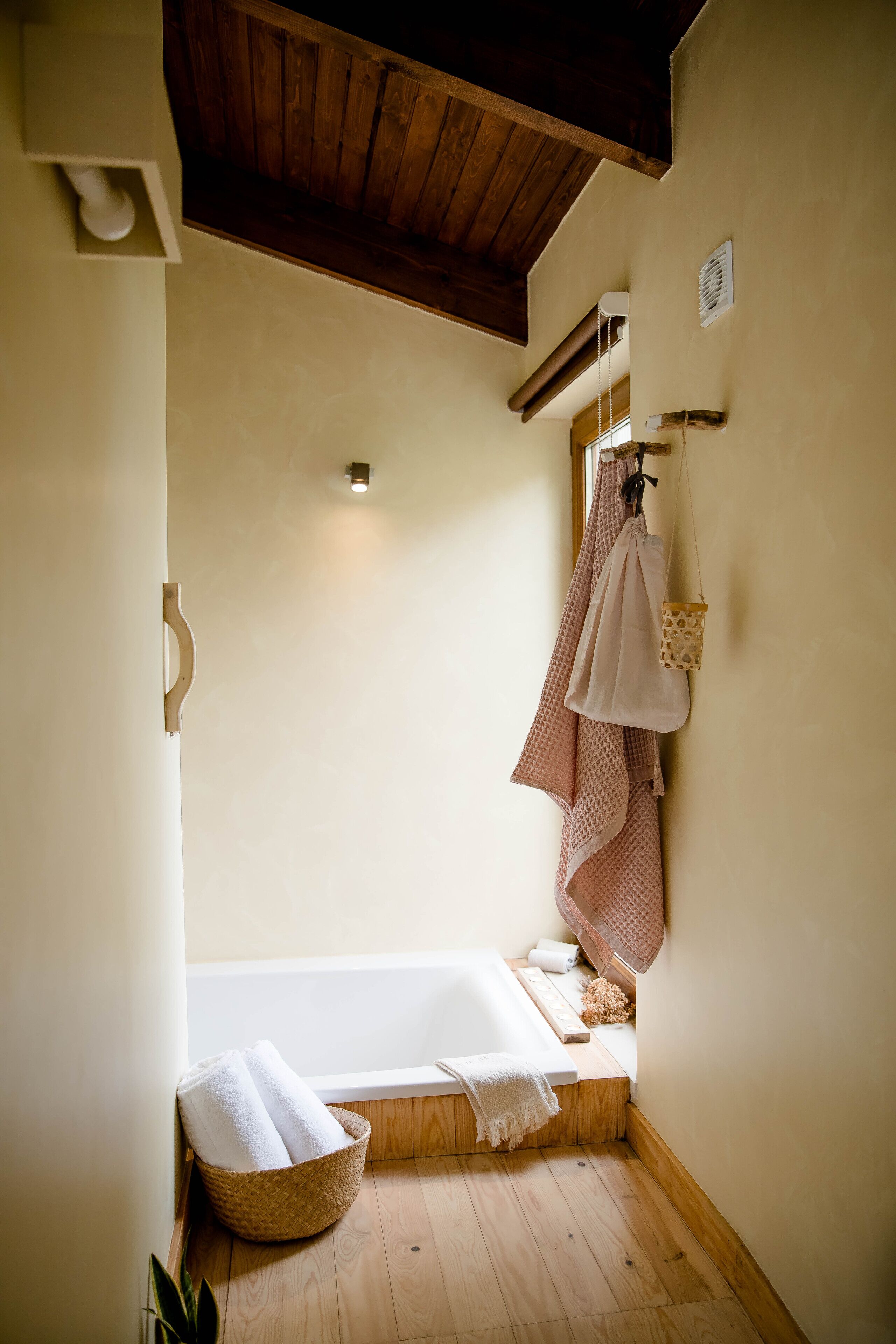 Un baño pequeño y acogedor con una bañera de madera, una cesta de mimbre con toallas y un perchero para toallas.