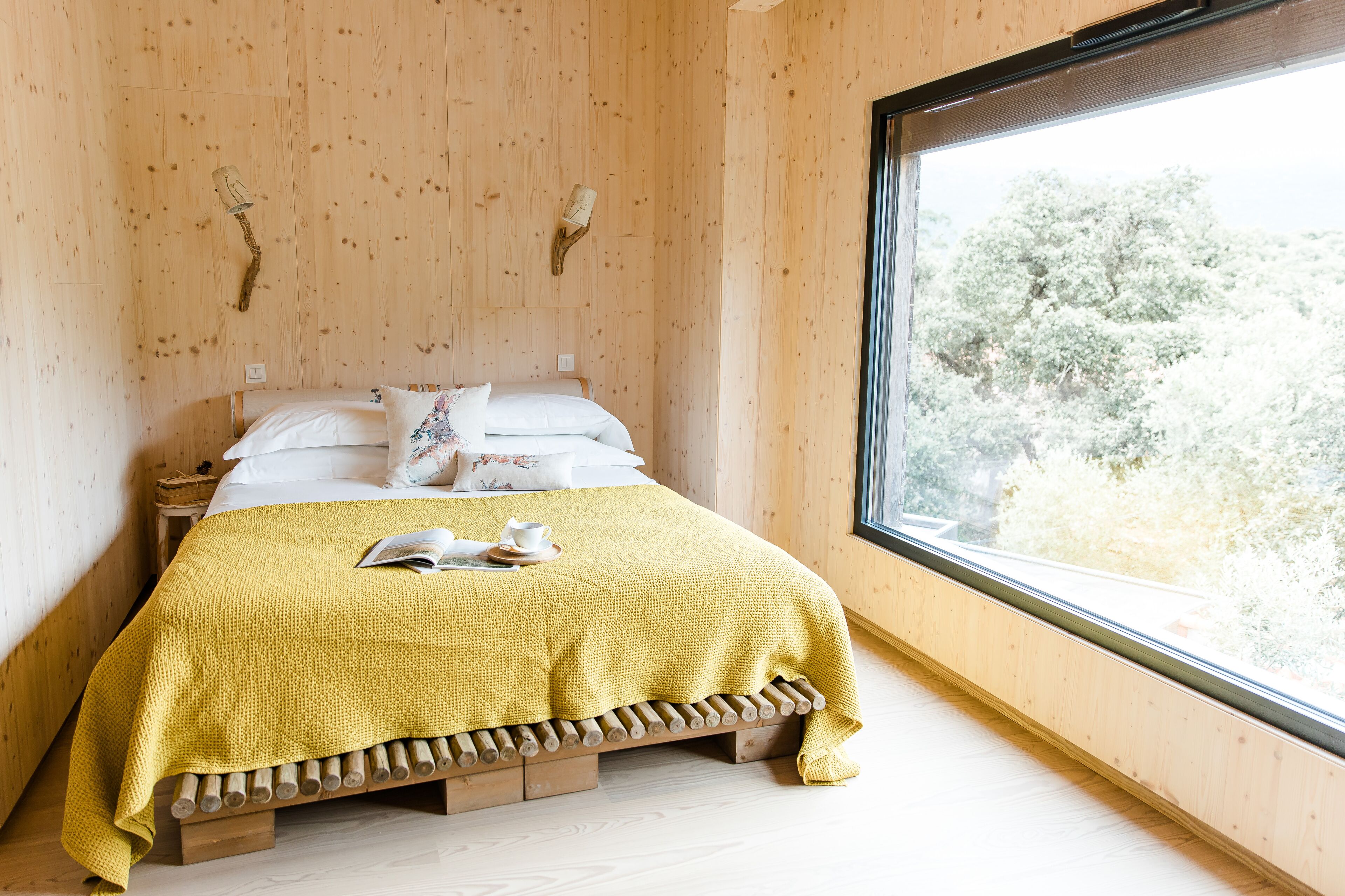 Una habitación con paneles de madera, una cama, un ventanal y vistas a árboles.