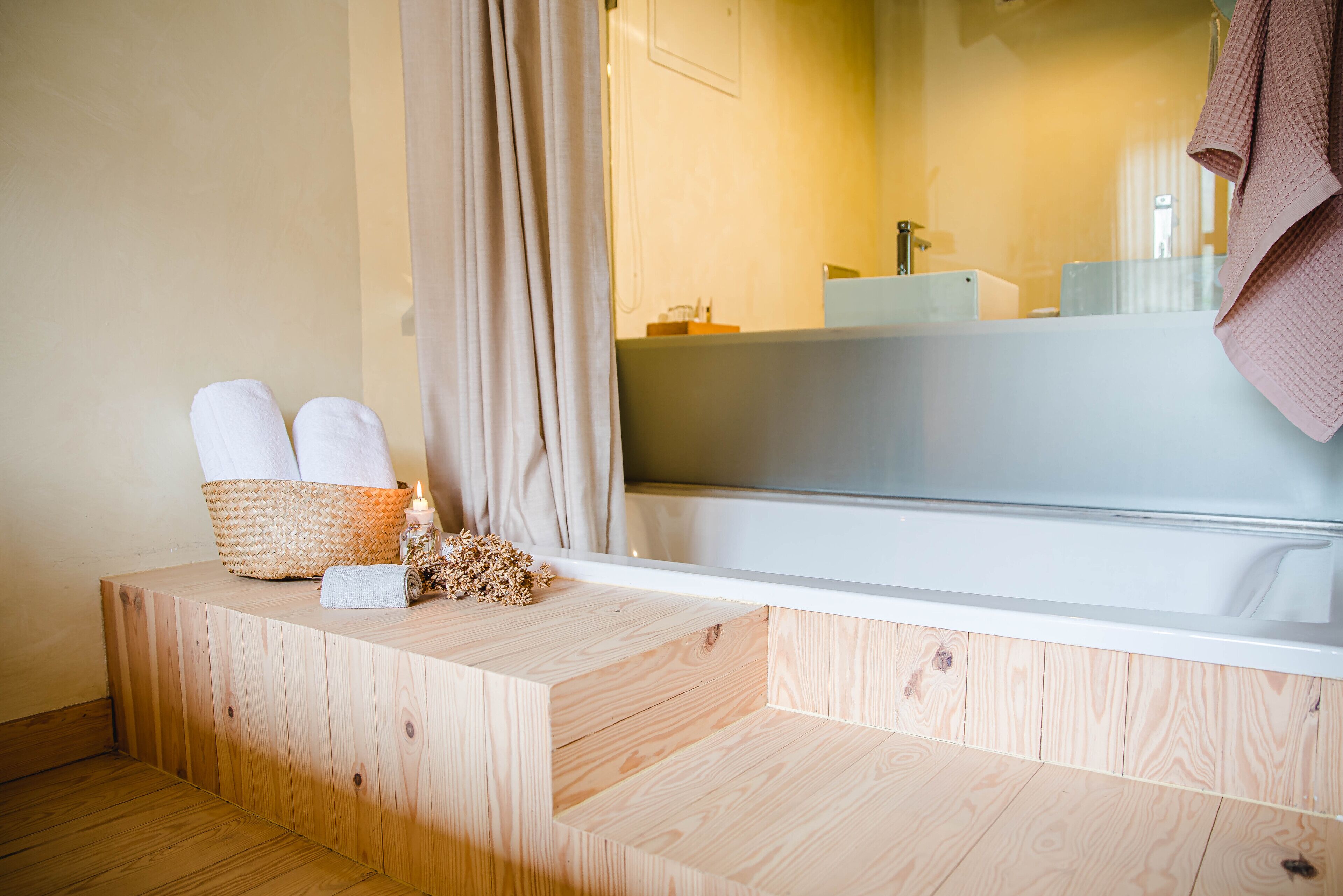 A wooden bench with towels and a basket, a bathtub, and a mirror reflecting a towel.