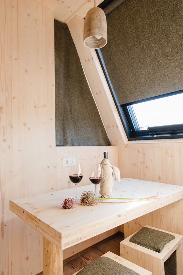 A wooden interior with a sloped ceiling, a table with two glasses of red wine, a candle, and a small plant.