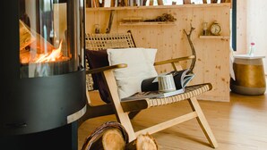 Une pièce chaleureuse avec un poêle à bois, un fauteuil confortable et une fenêtre donnant sur les arbres.