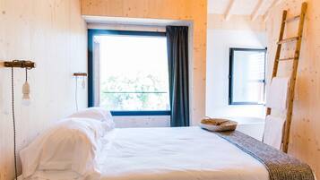 A wooden-paneled room with a bed, a window with curtains, a ladder, and a hanging light fixture.