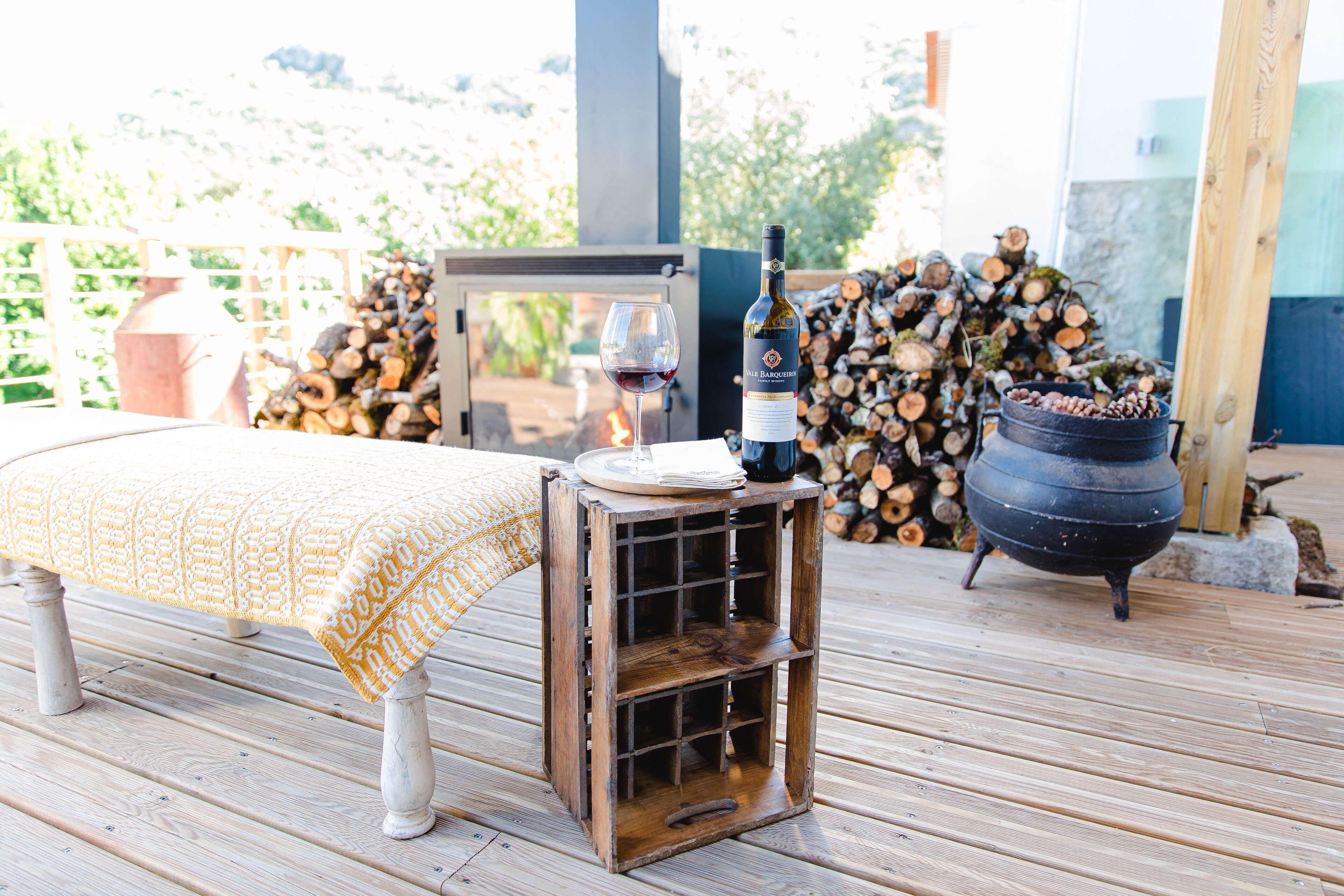 A wooden deck with a table and bench, a wine bottle, and a glass on the table.
