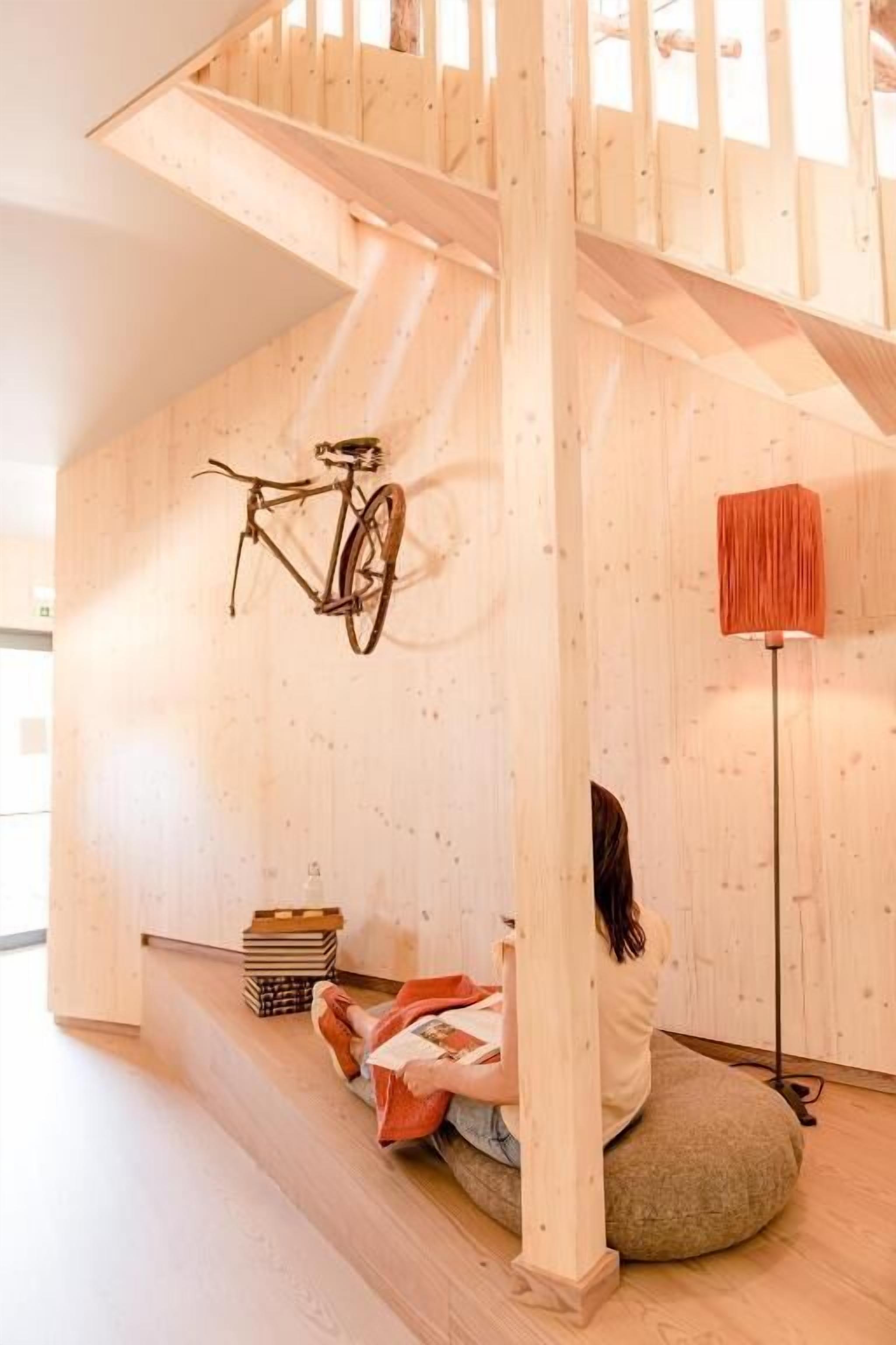 Ein Zimmer mit einer Holztreppe, einem hängenden Fahrrad, einer Stehlampe und einer Person, die auf einem Sitzsack sitzt.