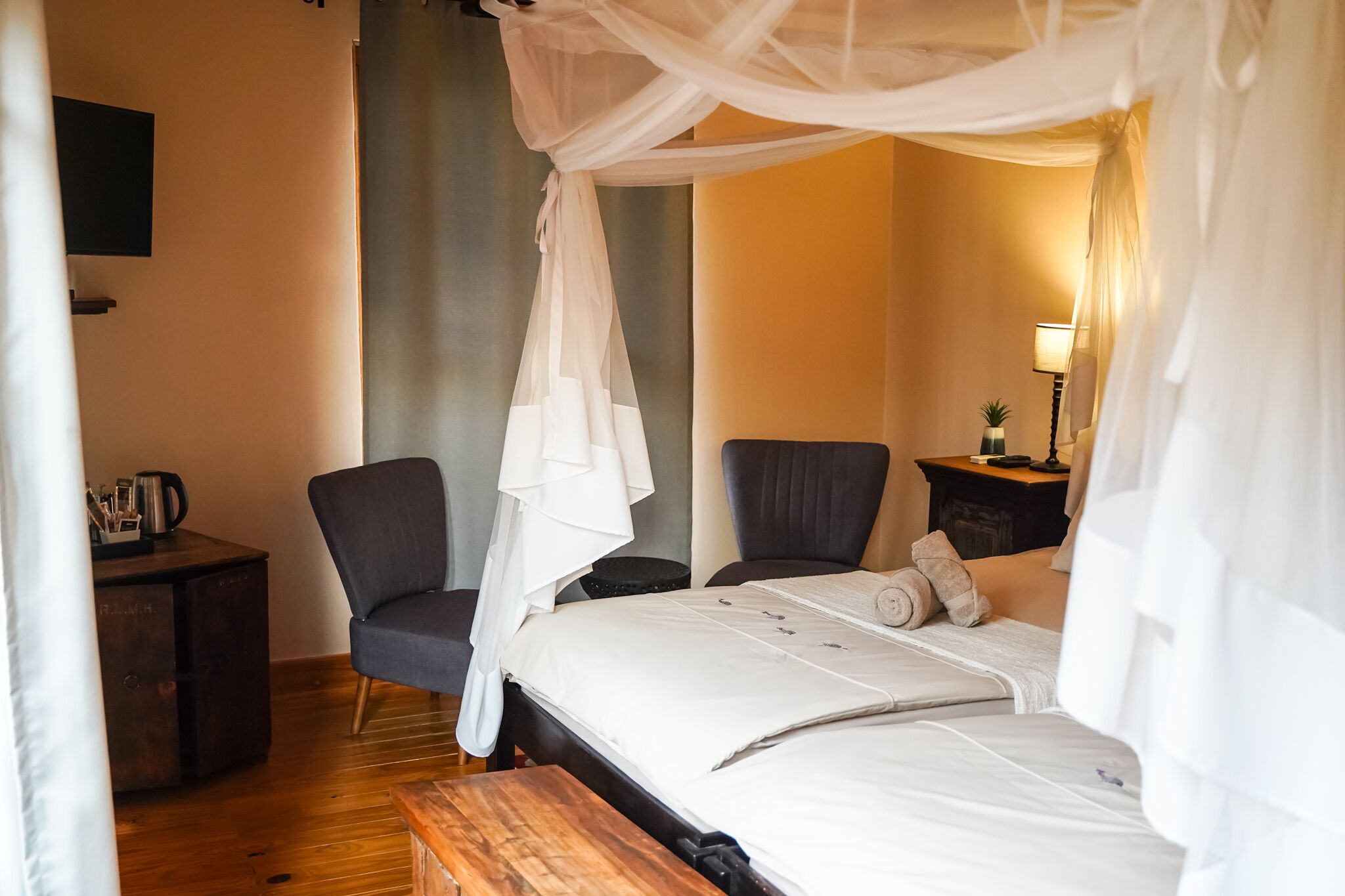 A bedroom with a bed under a canopy, a desk with a chair, and a bedside table with a lamp and a small plant.