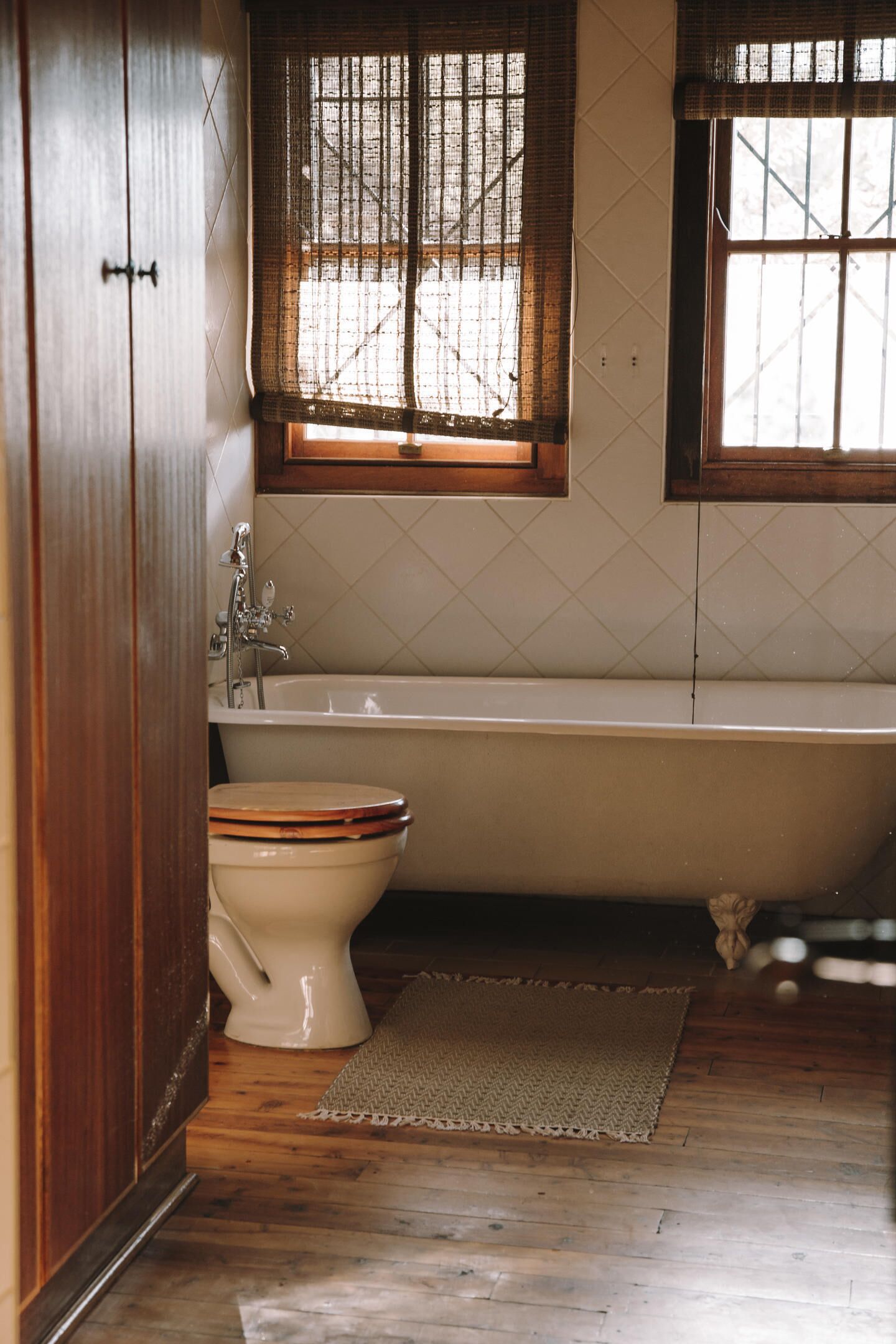 Un baño con piso de madera, una bañera, un inodoro y un ventanal con vistas a árboles.