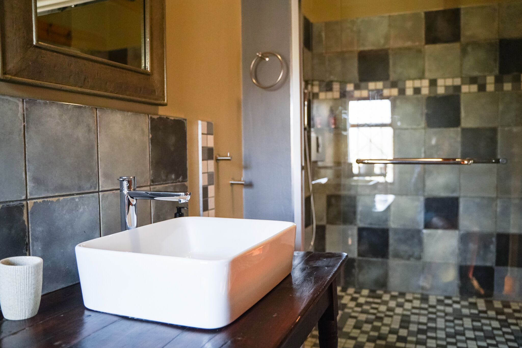 A bathroom with a white sink, dark tiles, and a glass shower enclosure.