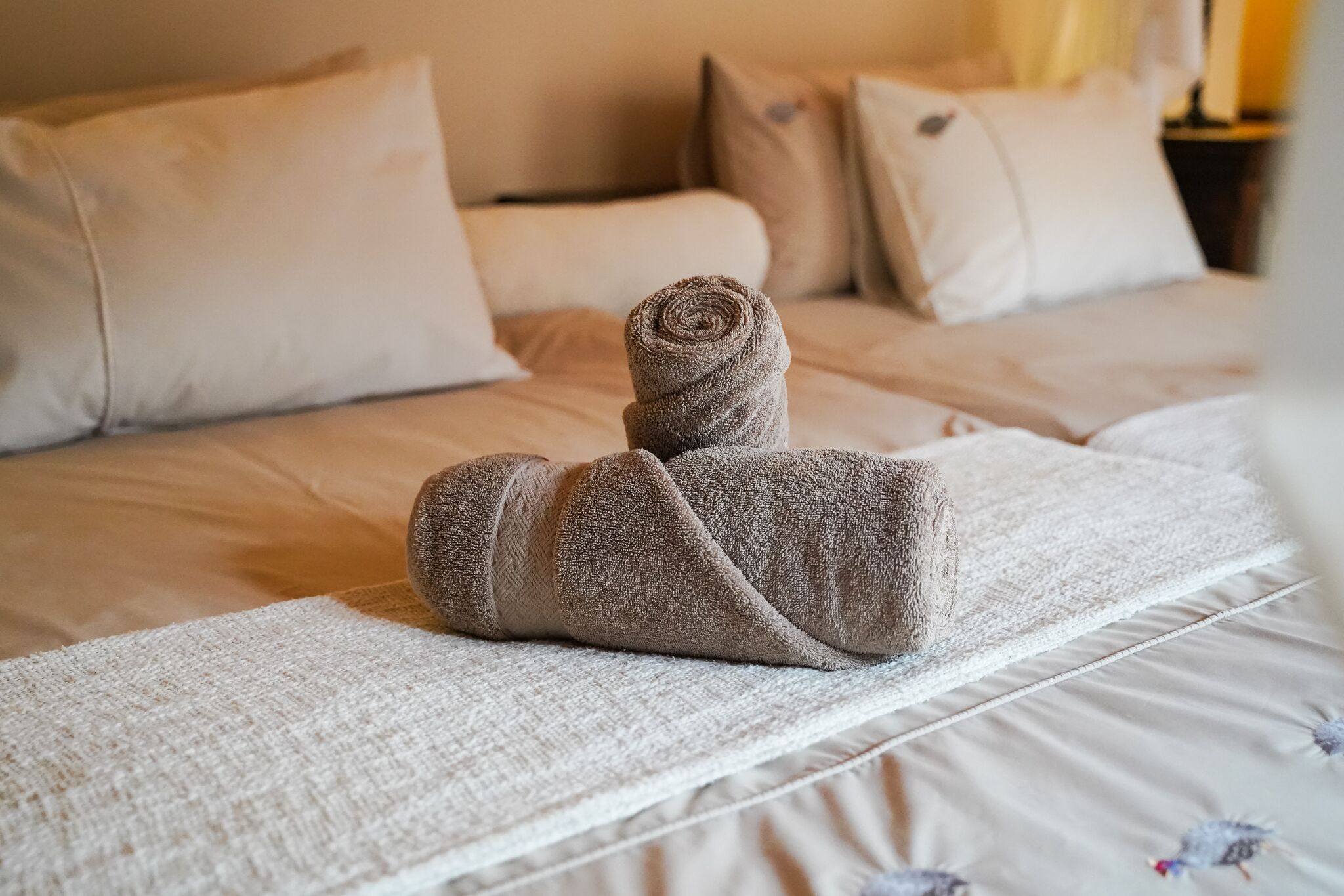 Un lit bien fait, avec une serviette enroulée et une couverture blanche à texture intéressante.