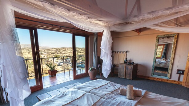 A bedroom with a large bed, a balcony, a potted plant, and a mirror. - Ti Melen Boutique Guesthouse l Ondili (Windhoek)