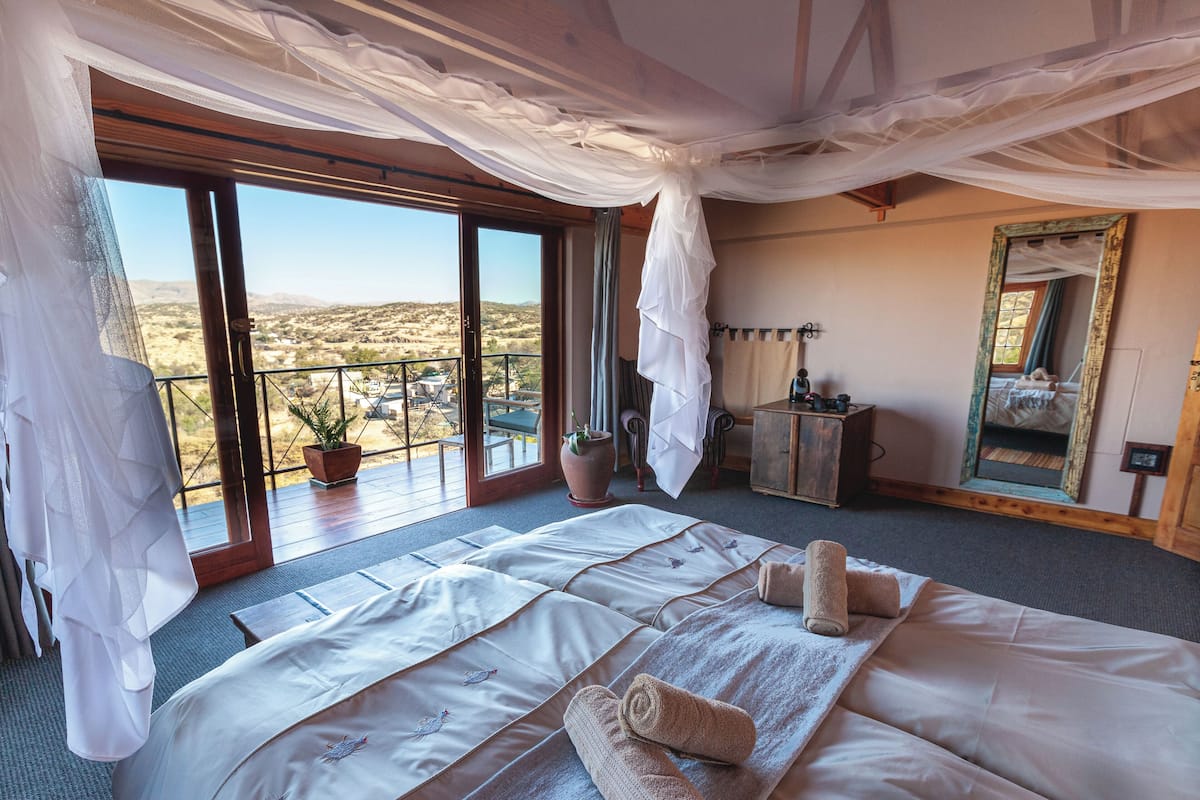 A bedroom with a large bed, a balcony, a potted plant, and a mirror.