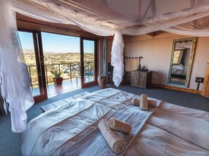 Ein Schlafzimmer mit einem großen Bett, einem Balkon, einem Topf mit einer Pflanze und einem Spiegel.
