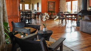 A spacious room with wooden flooring, a dining area with multiple chairs, a sofa, and a small table with a flower vase. - Ti Melen Boutique Guesthouse l Ondili (Windhoek)