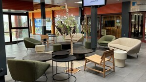 Un área de estar interior moderna con mesas y sillas redondas, una pantalla de televisión grande y un mostrador de recepción de madera.