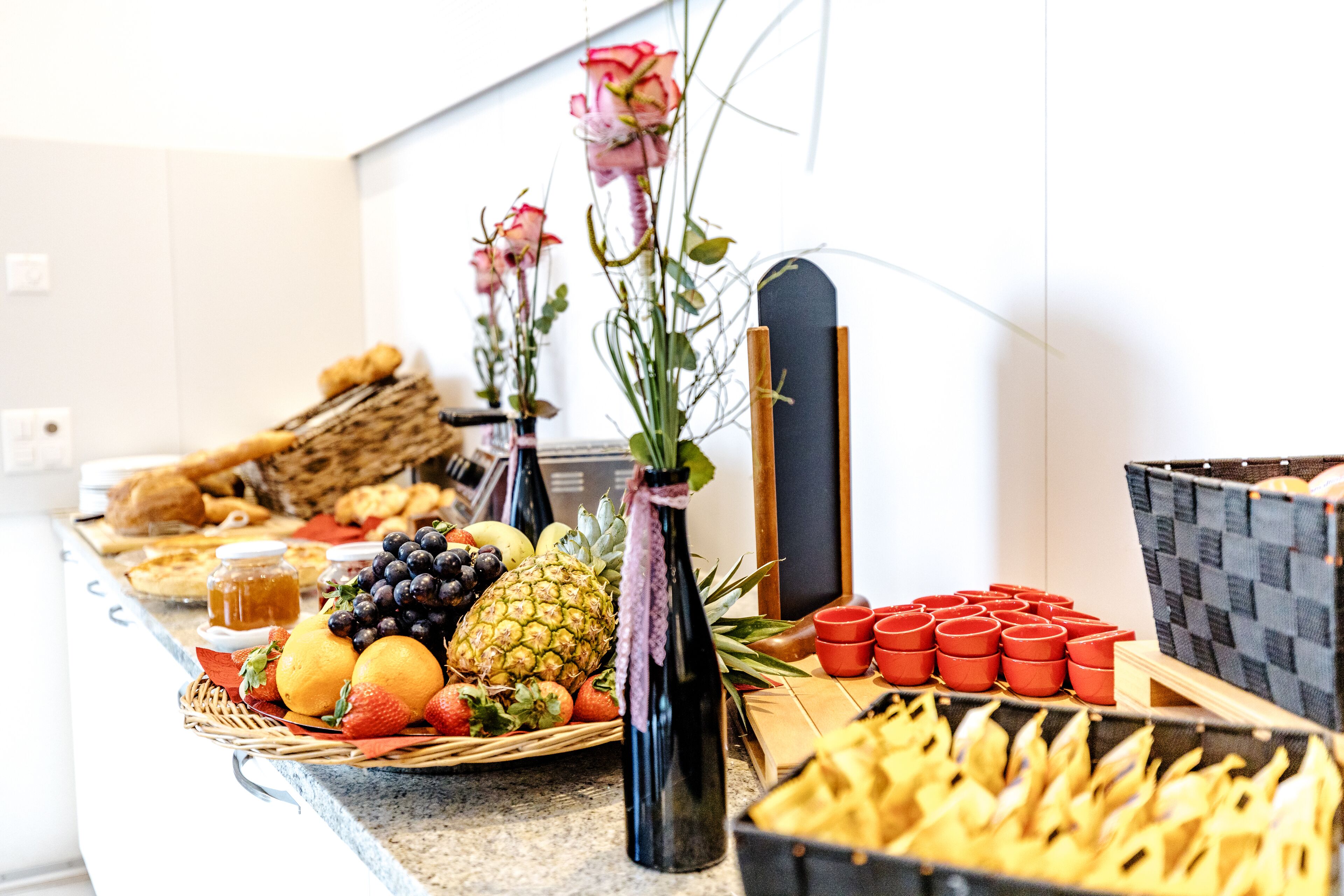 A buffet table with various fruits, pastries, and a vase with flowers.