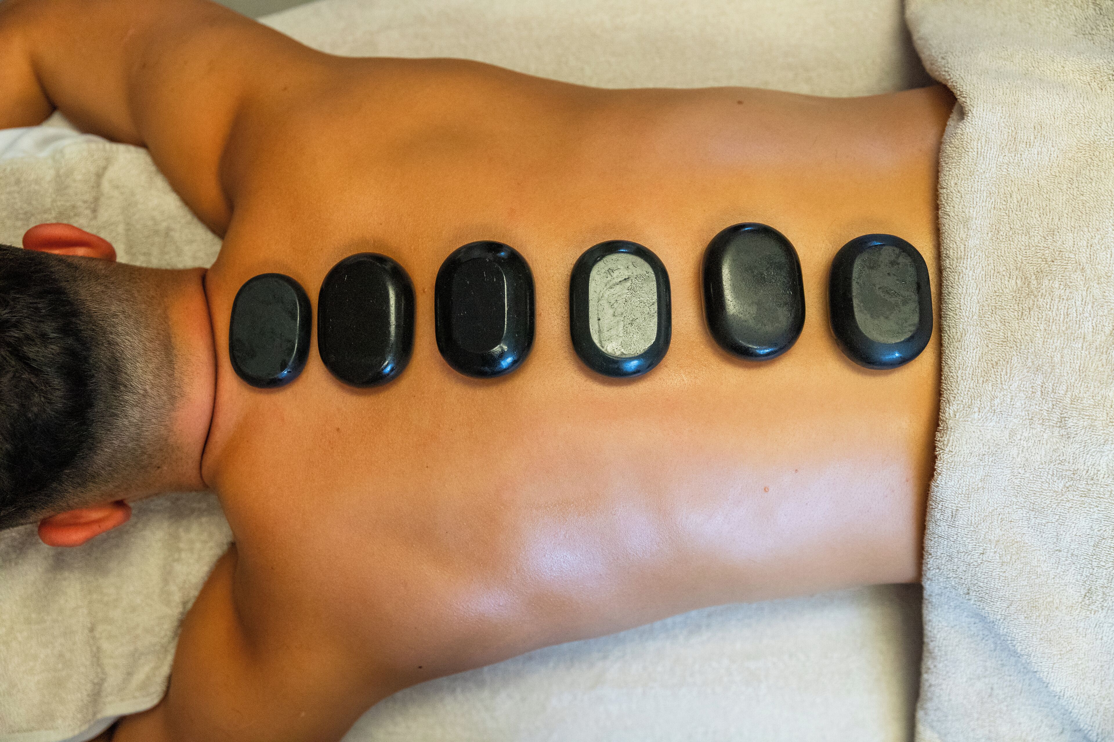 A person receiving a back massage with black stones placed along their spine.