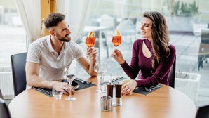 Una pareja sentada en una mesa con copas de vino, un vaso de agua y saleros y pimenteros.
