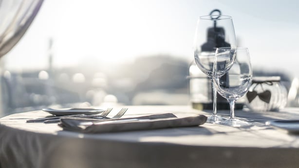Una mesa servida con una copa de vino, un tenedor y un cuchillo, con vista a la ciudad al fondo.
