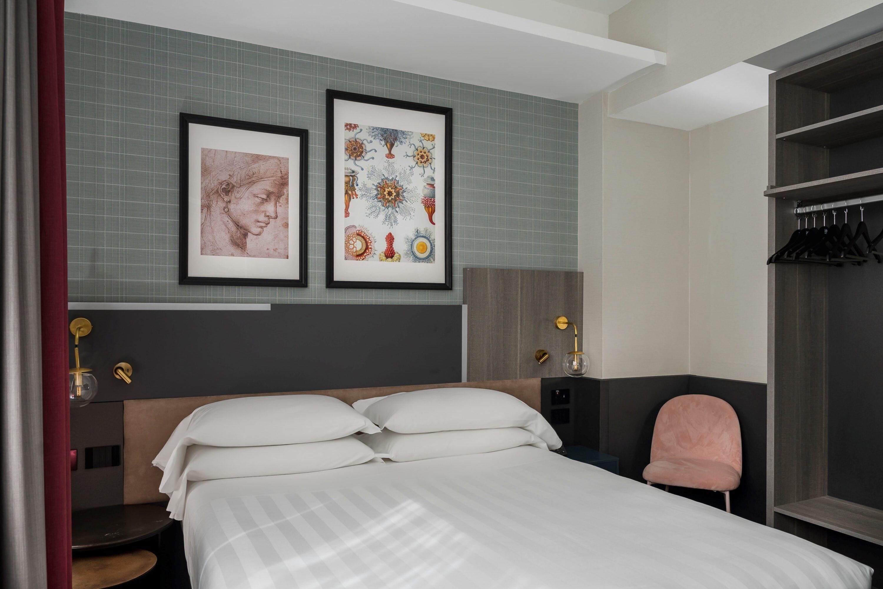 Una habitación de hotel moderna con una cama grande, un área de descanso, un armario y dos obras de arte enmarcadas en la pared.