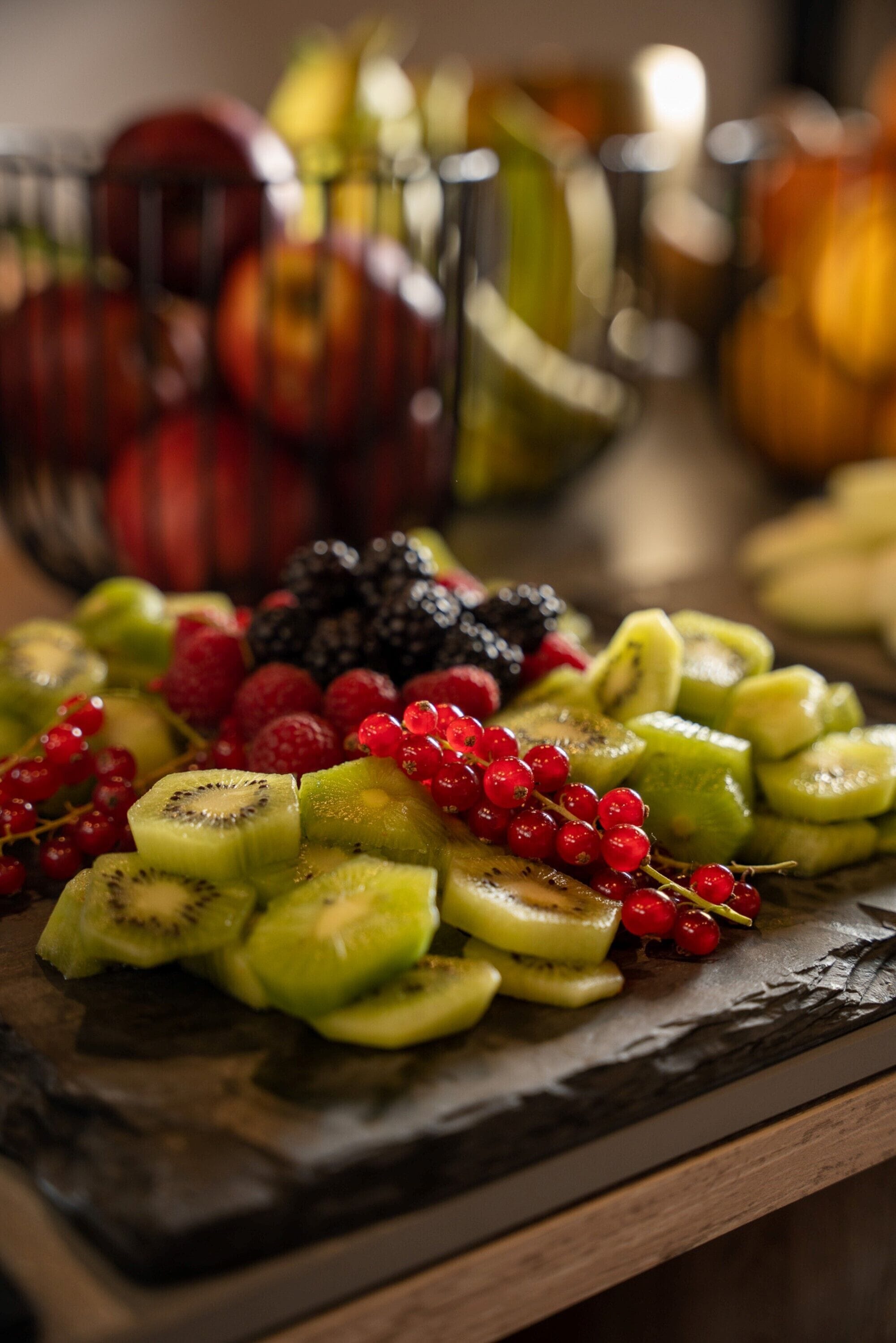 A fruit platter with sliced kiwi, red currants, and blackberries on a slate board.