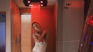 Una persona de pie en una ducha con luz roja, una puerta de madera y un pared con azulejos.