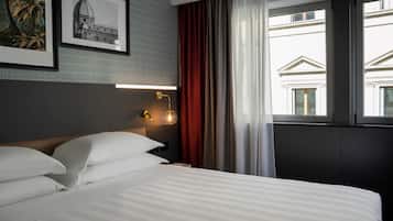 Una habitación de hotel con una cama bien hecha, una lámpara de pared y un ventanal con cortinas.
