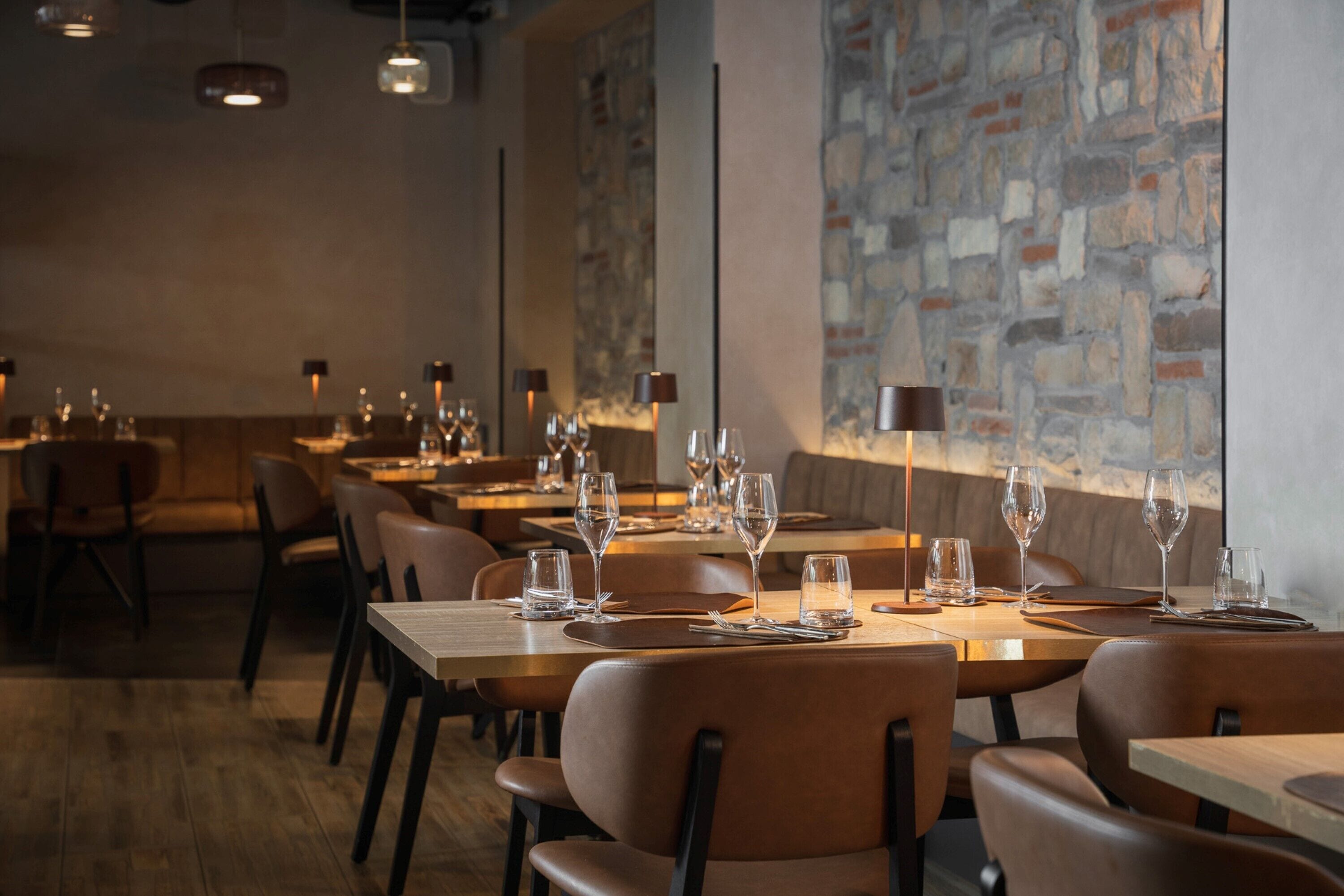 Una sala ristorante con tavoli e sedie in legno, ogni tavolo apparecchiato con calici e posate.