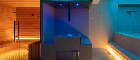 Uma sauna moderna com interior em madeira, estrutura de vidro e teto iluminado em azul.
