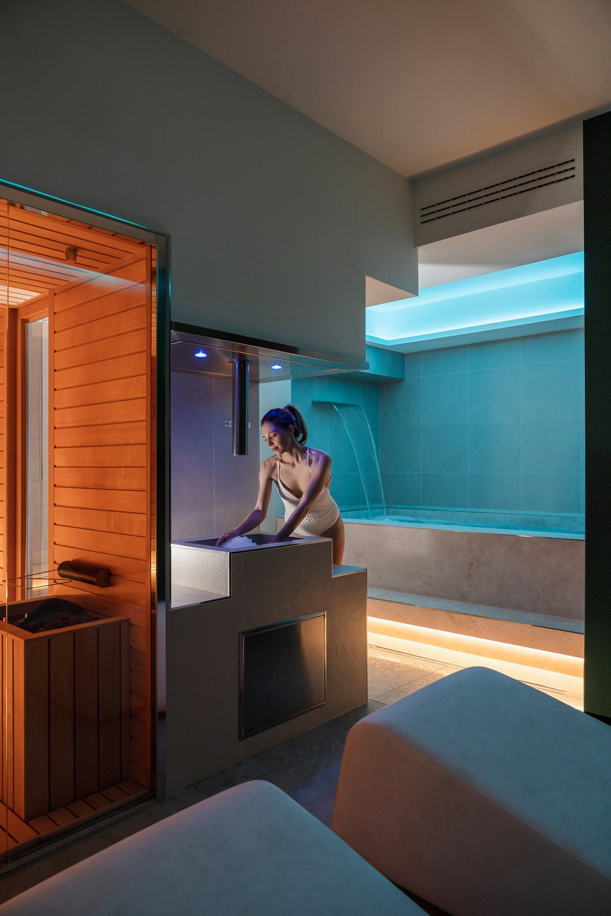 A modern spa room with a wooden sauna, a massage table, and a large bathtub.