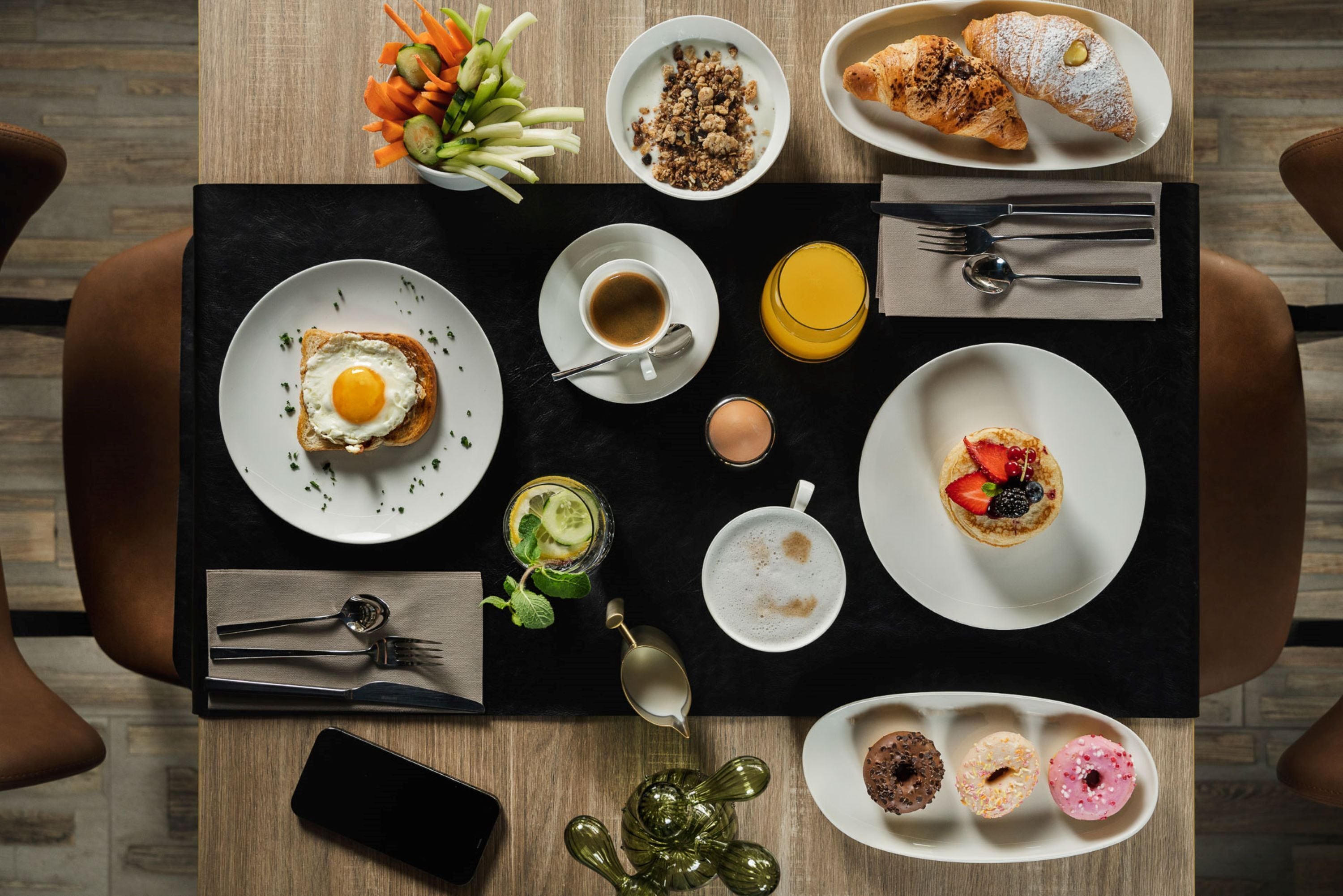 Ein Frühstücksbuffet mit verschiedenen Speisen, darunter Eier, Gebäck und Obst, auf einer schwarzen Tablett.