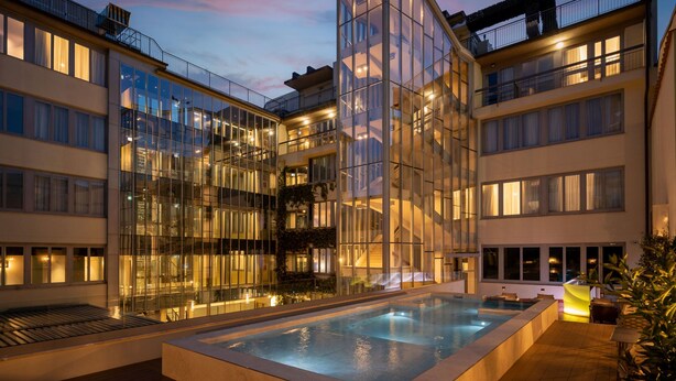 Un hotel moderno con fachada de vidrio, piscina en la azotea y varios balcones.